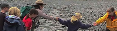 Ranger and teacher assist students crossing a stream