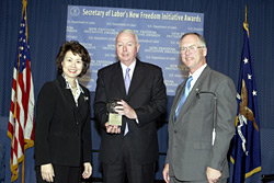 Secretary of Labor Elaine L. Chao (L) and Assistant Secretary of Labor for Disability Employment Policy Roy Grizzard (R) present a 2003 Secretary of Labors New Freedom Initiative Award to Dr. Ralph Shrader, CEO, Booz Allen Hamilton.  (DOL Photo/Shawn Moore)