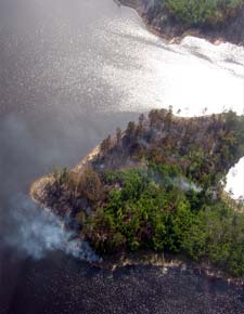 photo: Smoke and burnt trees on island in middle of lake.