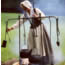 Female dressed in 18th century clothing cooking by outdoor fire.