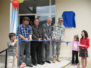 USAID Assistant Administrator Menarchik (3rd from left) joins members of the Vica community and Brig. General Douglas Earhart (far right), in cutting the ribbon to open a new primary school in Vica.