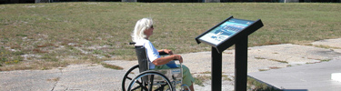 A woman in a wheelchair reads an outdoor wayside exhibit inside Fort Pickens.
