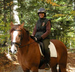 A smiling park volunteer sits astride a brown horse.