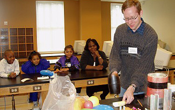 Researcher is about to smash a banana while several children and an adult watch the demonstration.