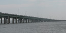 The uppermost level of a long bridge sloping down to the island is covered by a string of cars and vans.