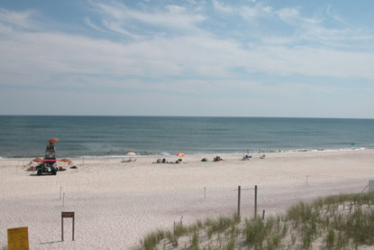 Blue sky with puffy white clouds over uncrowded lifeguarded beach along calm ocean.