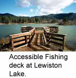 [photo]. Shows the accessible fishing deck at Lewiston Lake. The deck is the in the foreground. Lewiston Lake is midground, and tree covered hills are in the background. The sky is partially covered with clouds. Select for a larger photo.