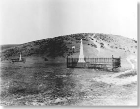 Historic photo of two wrought iron fence enclosed grave plots each with a tall monument.