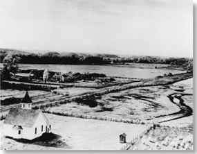 Historic photo with church in foreground and farmland behind.
