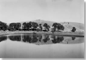 Millpond filled with water. Reflection of the hill and trees at the base of the hill can be seen on the pond's surface.
