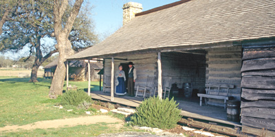 Volunteers in 1860s clothing stand on the porch of the Johnson Settlement cabin