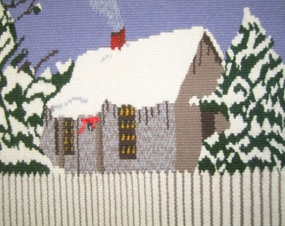 Hand-woven tapestry of a small wooden cottage behind a picket fence with a snow covered roof and flanked by snow-frosted trees.