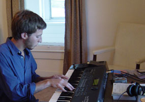 A young man wearing a blue shirt plays on an electric keyboard.
