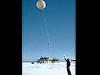 A man standing in an icy location releases a large weather balloon