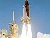 A space shuttle, surrounded by billowing white clouds of smoke, launches into the air