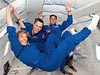 Three educator astronauts in blue flight suits floating in an airplane