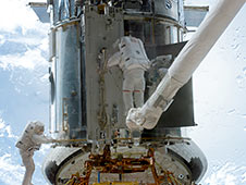 Astronauts working on the Hubble. One is on the robotic arm.