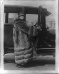 Mary LaFollette, full-length portrait in long raccoon coat, getting into auto in front of Capitol.