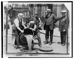 [Deputy Police Commissioner John A. Leach, right, full-length portrait, standing, facing right, watching agents pour liquor into sewer following a raid during the height of prohibition]