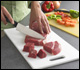 Raw meat being cubed on one cutting board; vegetables sliced on another cutting board.