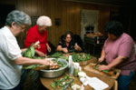 A group of women around a table, cleaning vegetables.
