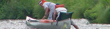 Rear view of two canoeists wading and pulling their canoe over a shallow spot