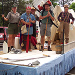 A parade float carrying a national park ranger, fur trader, hiker and logger