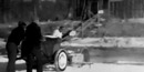 two men with a circular ice saw.  In the background blocks of ice are moving up a ramp into an ice house