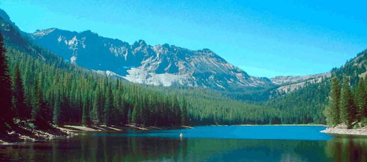 Photo of Strawberry Lake on the Malheur National Forest showing lake and trees in the foreground, against a background showing a blue sky and mountains.