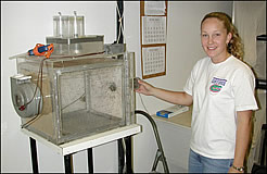 Photo:  young woman next to a  clear, rectangular case holding mosquitoes.