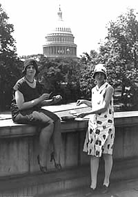 Photo: two women  with a frying pan on a concrete wall,.  U.S. Capitol in the background,