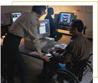 Man in wheelchair at computer with a woman coworker looking on