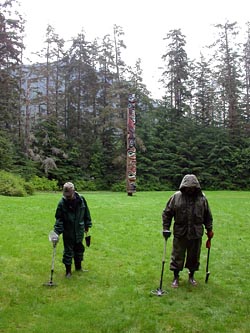 [photo] Two archeologists scan field with metal detector.