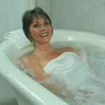color photo of woman reclining in ceramic tub with water bubbling from whirlpool, wearing a towel