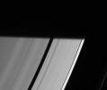Pan prepares to be engulfed by the darkness of Saturn's shadow, visible here as it stretches across the rings