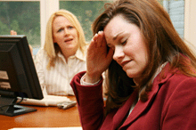 A photo of business woman looking stressed with an angry business woman in the background.