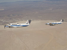 Two Beechcraft King Air mission support aircraft operated by NASA's Dryden Flight Research Center fly in formation over Rogers Dry Lake at Edwards AFB.