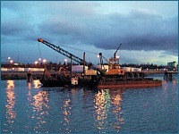 A dredge barge working in a channel at night.