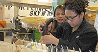 Girl uses hand tool while another girl looks on