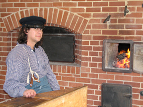 Site volunteer dressed a a soldier assigned to braad making duty.  Here he is tending the fire.  Breadmaking will be one of the activities going on at the Fort during Memorial Day weekend.