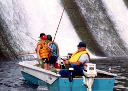 Photo of three men and a child fishing in a boat in front of a waterfall