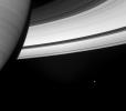 Beside the swirling face of Saturn floats a small, icy attendant