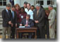 President George W. Bush signs the Job Creation and Worker Assistance Act of 2002 during a live radio address in the Rose Garden March 9, 2002. On hand for the signing were Senators Trent Lott (far left) and Tom Daschle (second from left) and Speaker of the House Dennis Hastert (standing to right of the President). "We're seeing some encouraging signs in the economy, but we can't stand by and simply hope for continued recovery," said President Bush. "We must work for it." White House photo by Eric Draper.