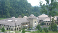 A photo of the Children's Inn at NIH, which is a large, two-story, gray-stone building that is surrounded by lawn and large trees. The Inn, which can accommodate 59 families, features several common-area living rooms, laundry facilities, a communal kitchen, television room, library, computer room, and play room.