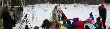 Students on a school field trip gather in the snow to learn what life was like in the past from costumed ranger/interpreters