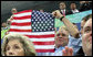 President George W. Bush displays an American flag as he cheers on the U.S. Olympic Swimming Team Sunday, Aug. 10, 2008, at the National Aquatics Center in Beijing. White House photo by Shealah Craighead