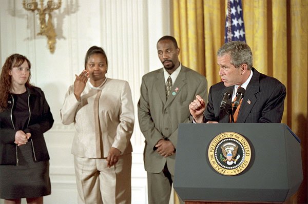 President George W. Bush discusses welfare reform as former welfare recipient Bernadine Murphy wipes away her tears in the East Room Thursday, April 18. Also standing by the President are Tiffany Smith and Emory Bent. "(Ms. Murphy) lived in a homeless shelter, too. She also struggled with drug abuse, and her self-esteem was, as she put it, "nonexistent." Bernadine enrolled in a 13-week training program, spent 11 weeks working part-time with a mentor," said the President, explaining that Ms. Murphy now lives in on her own and works at a law firm in Chicago. White House photo by Tina Hager.