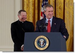 President George W. Bush addresses The National Catholic Educational Association in the East Room Friday, Jan. 9, 2004. The Association represents more than 200,000 educators serving 7.6 million students in Catholic education at all levels. Pictured with the President is His Excellency Gregory Aymond, Bishop of Austin, Texas.  White House photo by Tina Hager
