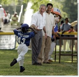 Shaquana Smith holds onto her hat as she runs to President George W. Bush and White House Tee Ball Commissioner Barry Larkin after her Memphis Red Sox played the Black Yankees of Newark during Sunday's "Tee Ball on the South Lawn."  White House photo by Paul Morse