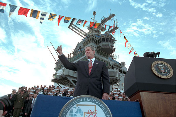 President George W. Bush salutes during his remarks at the USS Enterprise Dec. 7.  "I'm grateful for this warm welcome on the deck of the "Big E," said the President. "America is proud of this fine carrier and we're really proud of her crew.  You're serving at a crucial moment for the cause of peace and freedom, and your country thanks you."White House photo by Paul Morse.